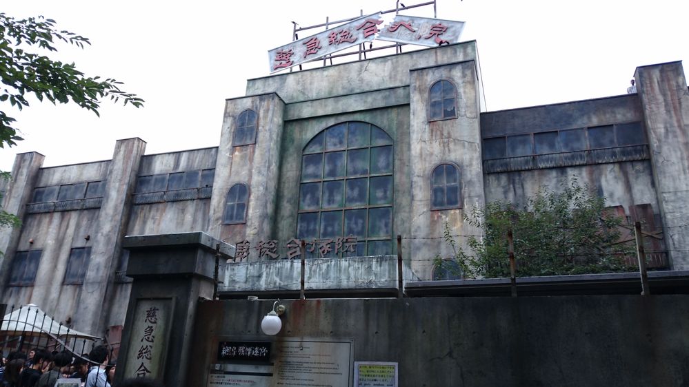 Caption: A photo of Japanese amusement park Fuji-Q Highland’s haunted house, which is a large building that is made to look decrepit hospital with high stone fences and barbed wire surrounding it. (Local Guide 木下和正)