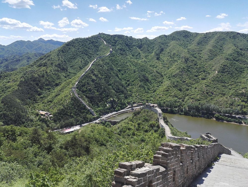 描述：一张中国长城在山上蜿蜒而下的照片，一条河在黄花城水长城的旁边。(本地向导  @TsekoV)