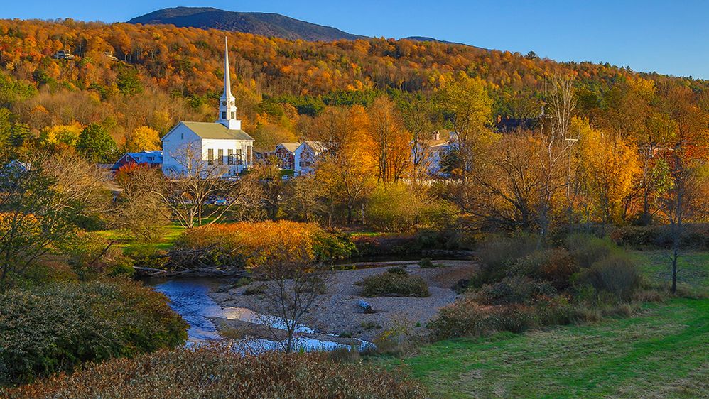 Caption: A photo of the Stowe Community Church with trees and a creek taken during autumn in Stowe, Vermont, USA. (Local Guide Charles Lee)