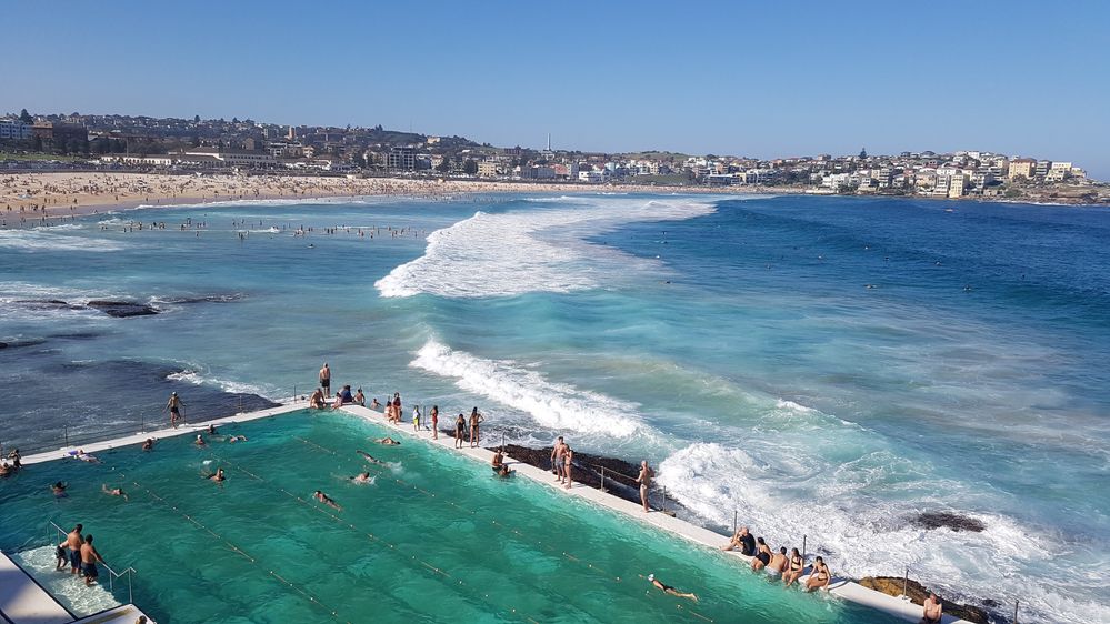 Caption: A photo of Sydney’s Bondi Icebergs Club, a swim club on Bondi Beach featuring pools that jut out over the ocean and are filled with seawater from the waves, along with the coastline and beach in the background. (Local Guide John Mulley)