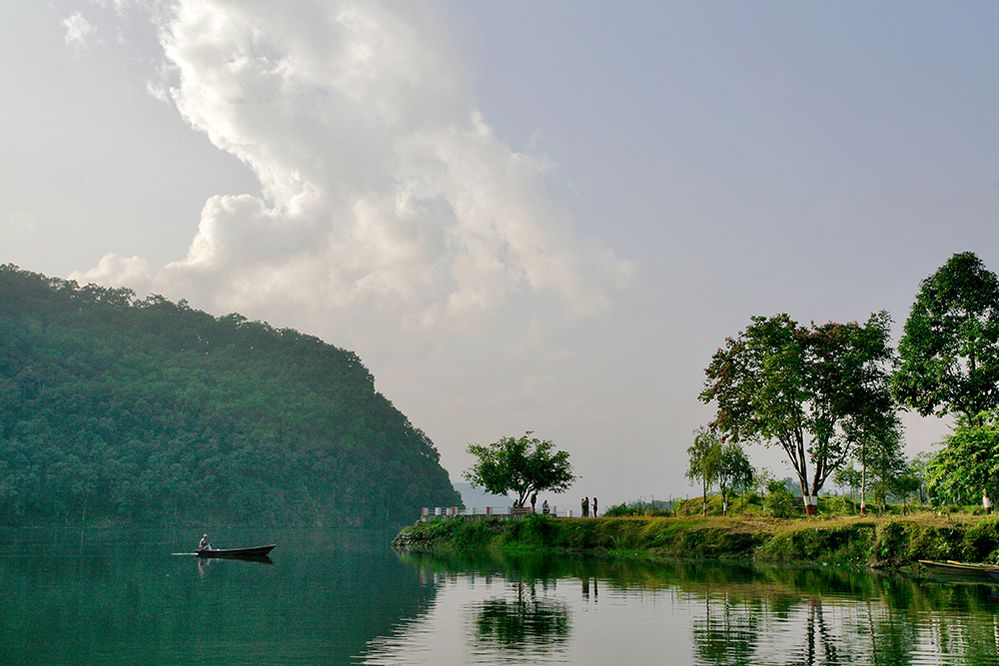 Caption: A photo of a person in a small boat on a lake next to a tree-lined waterfront in Basundhara Park, Pokhara, Nepal. (Local Guide Gibbon Neo)