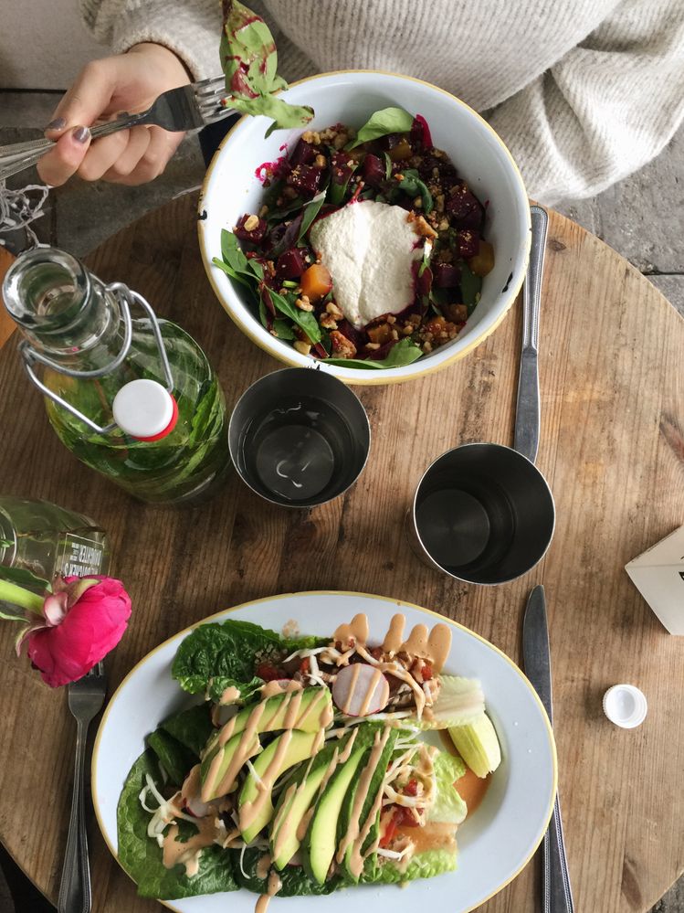 Caption: A photo of a person across the table from a vegetable dish, holding a fork over a bowl of salad at The Butcher’s Daughter, a vegetarian restaurant in New York City. (Local Guide Marcela Turner)