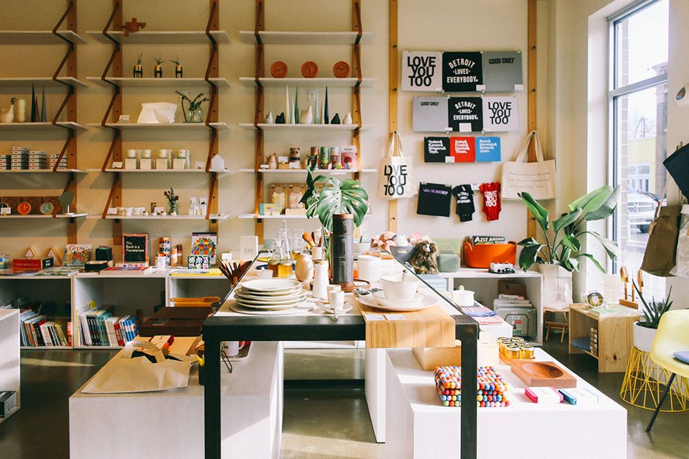 Caption: A photo of the interior of the home goods and gift store, Nora Detroit, with products, including t-shirts, tote bags, plates, and more, for sale on tables and shelving dotted with green plants. (Local Guide Arthurious)