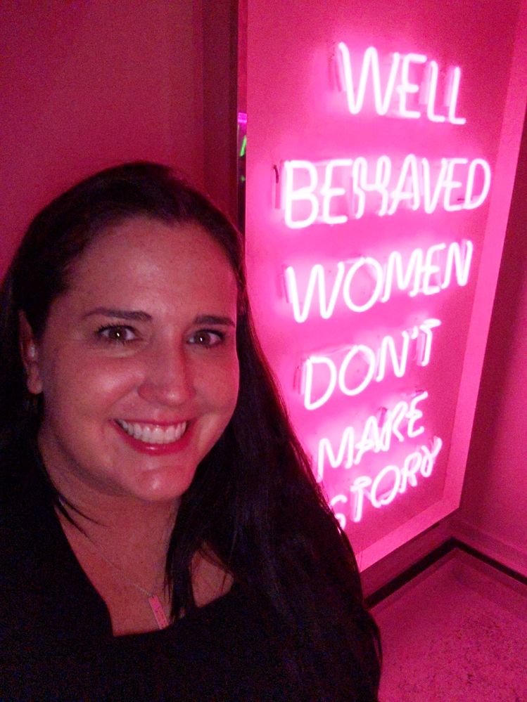 Photo Caption: Me in front of a pink neon sign that says "Well behaved women don't make history,.