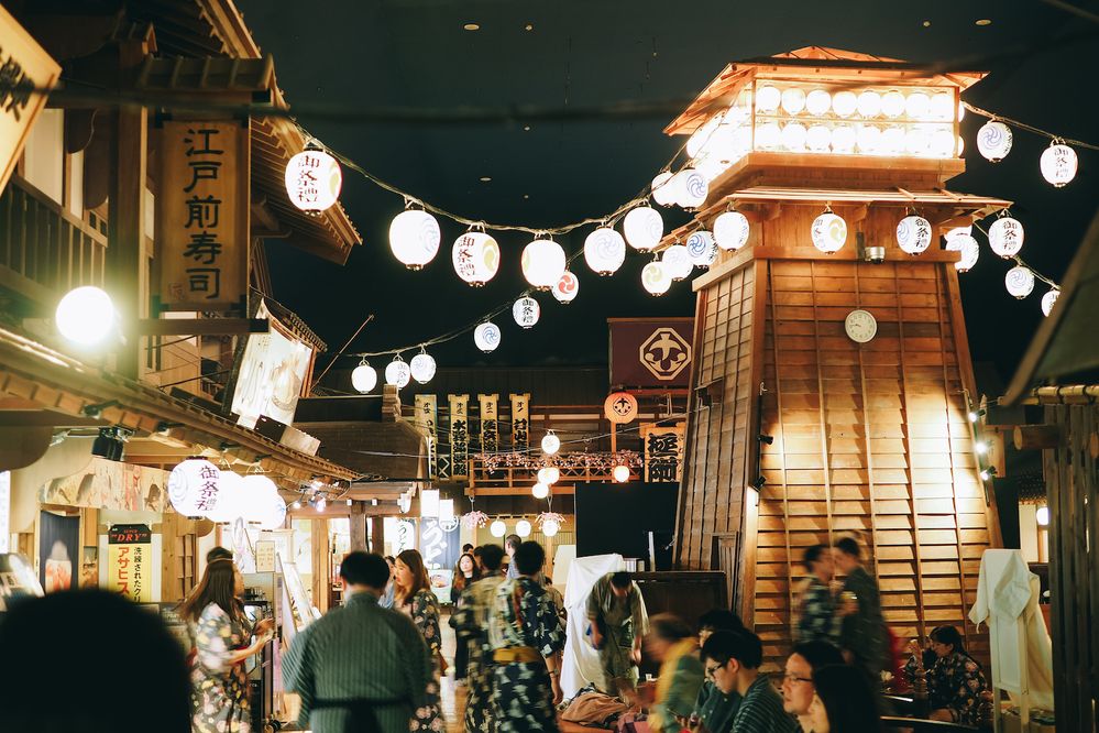 Caption: A photo of the inside of Tokyo Odaiba Oedo Onsen Monogatari at night filled with people and illuminated by lantern string lights. (Local Guide Kritsada Chatthama)