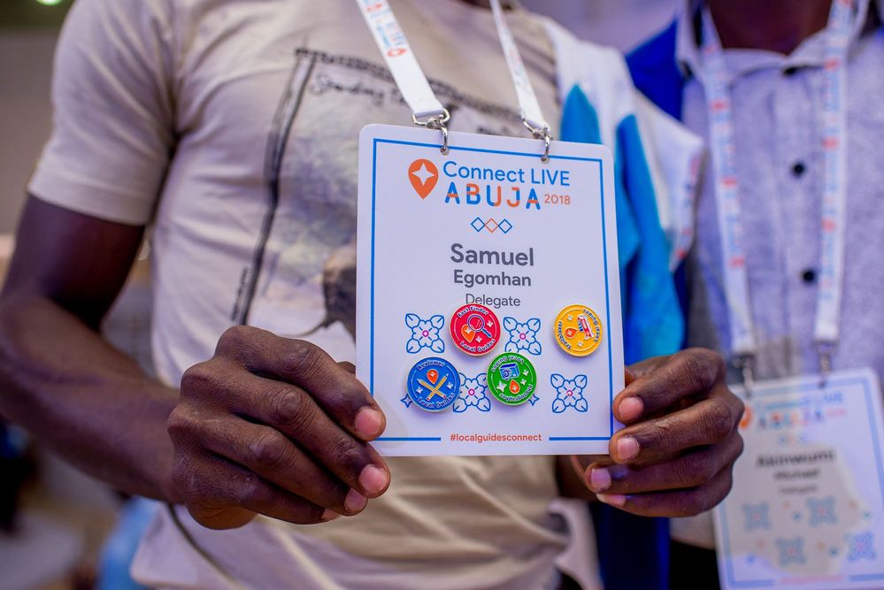 Caption: A photo of Local Guide Samuel Egomhan holding up a set of Local Guides collector’s pins attached to a lanyard that’s around his neck at Connect Live Abuja 2018.