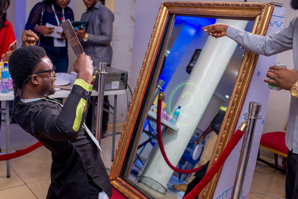 Caption: A photo of a Local Guide flexing his biceps while posing for the camera in front of a Mirror photo booth at Connect Live Abuja 2018. A countdown timer showing the number “2” is illuminated in green on the framed mirror.