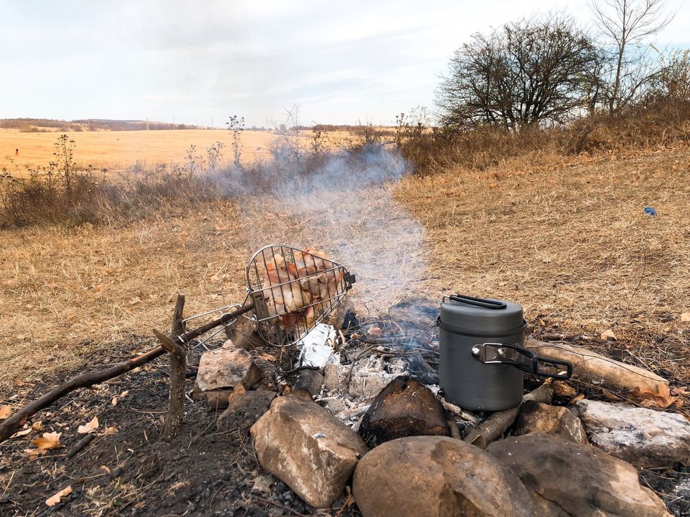 Caption: A photo of a hearth made of stones in an autumn field, with chicken pieces roasting in a grill net and a container for tea placed in the stones. (Local Guide @FelipePk)