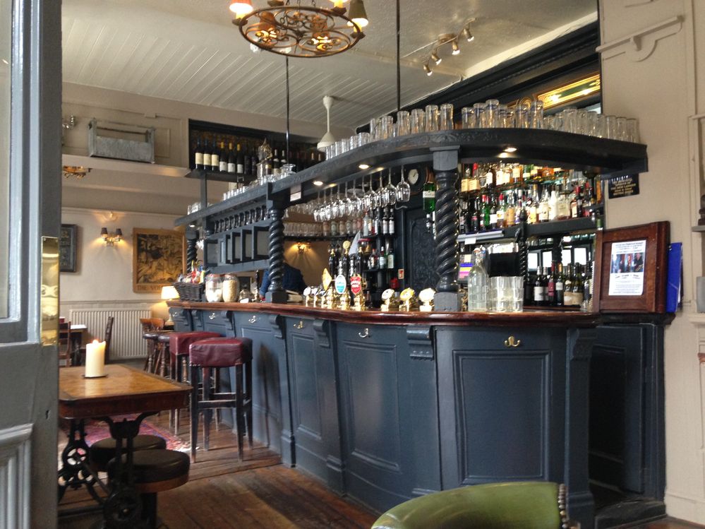 Caption: A photo of the interior of The Andover Arms, a pub in London, showing its blue-gray bar, wood tables and floor, and leather chairs. (Local Guide Christopher Clogher)