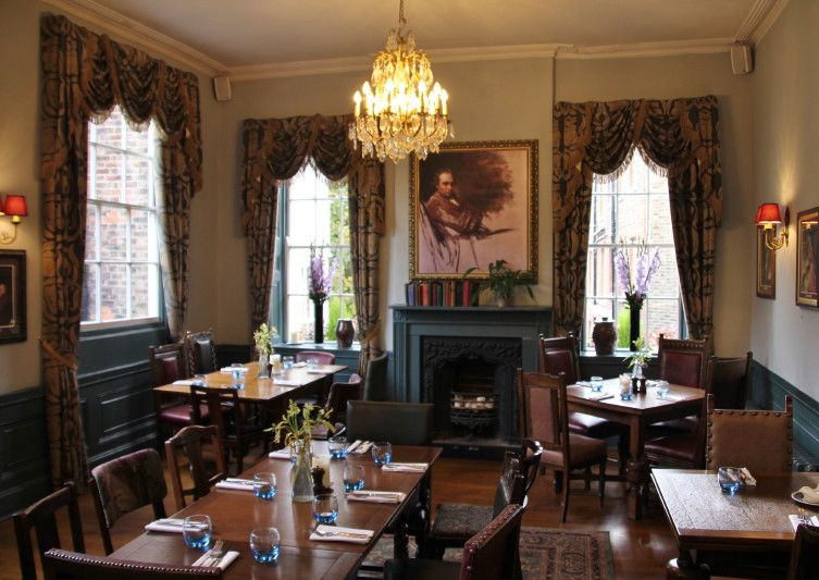 Caption: A photo of the cozy interior of The Holly Bush, a pub in London, showing its blue fireplace, wooden tables and chairs, heavy curtains, and chandelier. (Local Guide Alan Pembshaw)