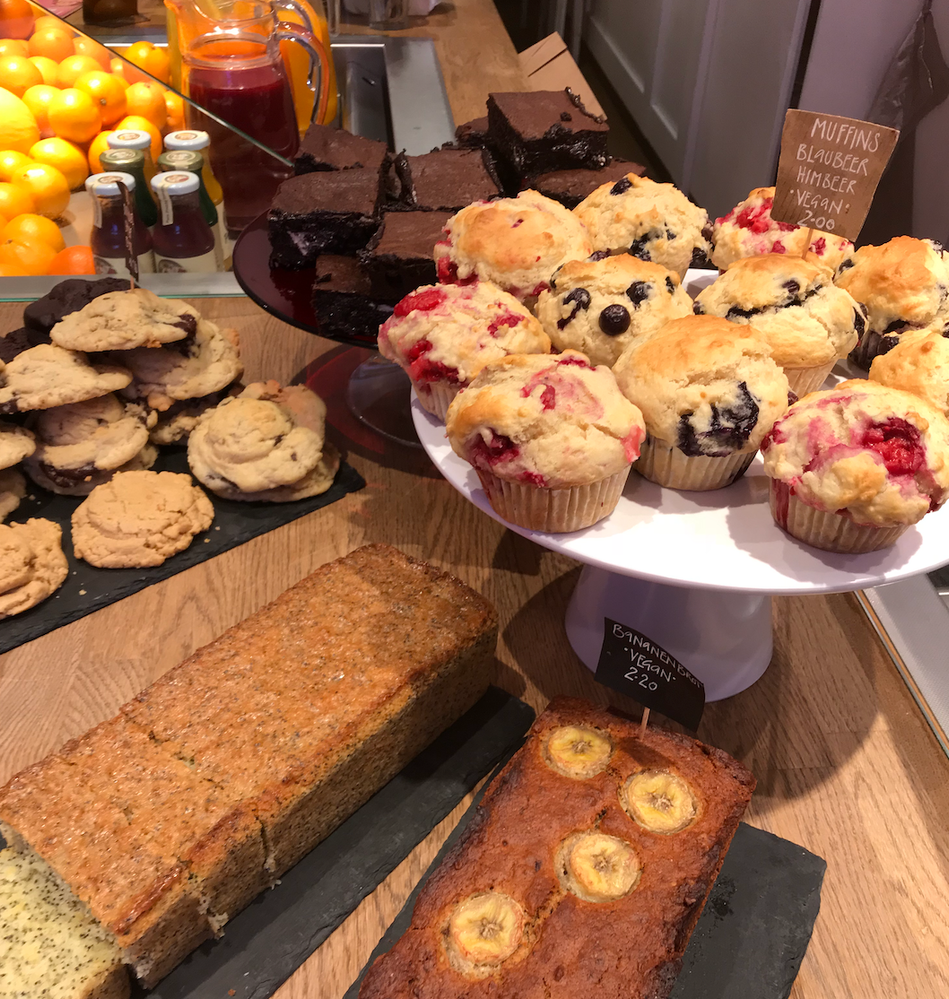 Caption: A photo of vegan baked goods on display for sale at a cafe in Berlin, Germany. The baked goods include vegan blueberry and raspberry muffins, vegan banana bread, cookies, brownies, and poppyseed bread. (Local Guide @MiaMaria)