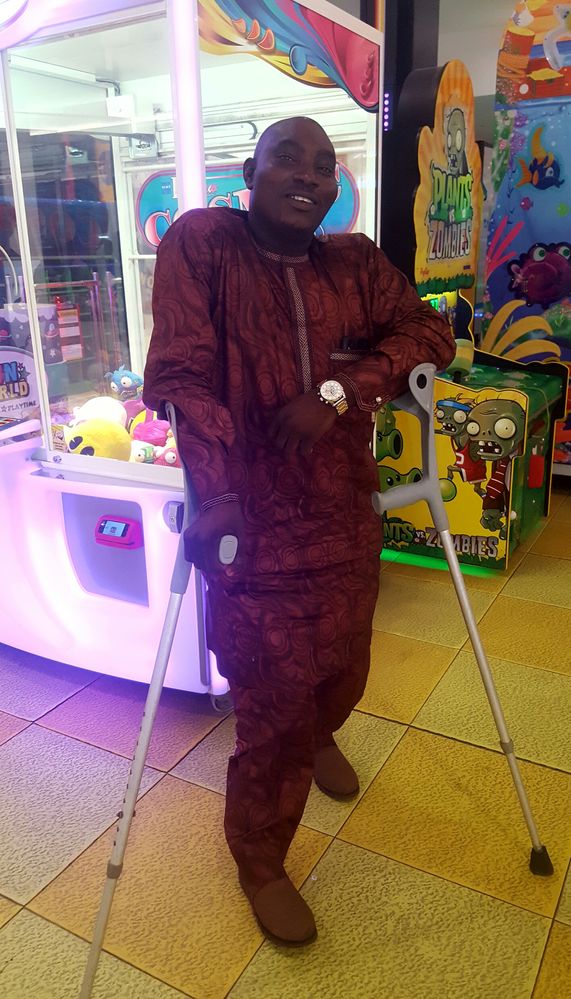 Caption: A photo of Emeka's friend John wearing a brown kaftan with crutches on both hands during a recent meet in Lagos