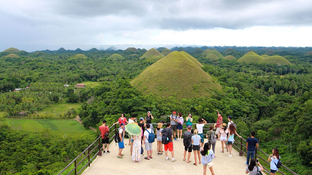 Caption: A photo of a tourists taking photographs while standing on a lookout over hills at the Chocolate Hills Complex in Bohol, Philippines. (Local Guide mnger mnger)
