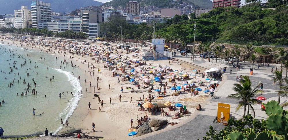 Caption: A photo of Ipanema Beach in Rio de Janeiro packed with sunbathers and swimmers, surrounded by the city and nearby mountains. (Local Guide andres aranda)