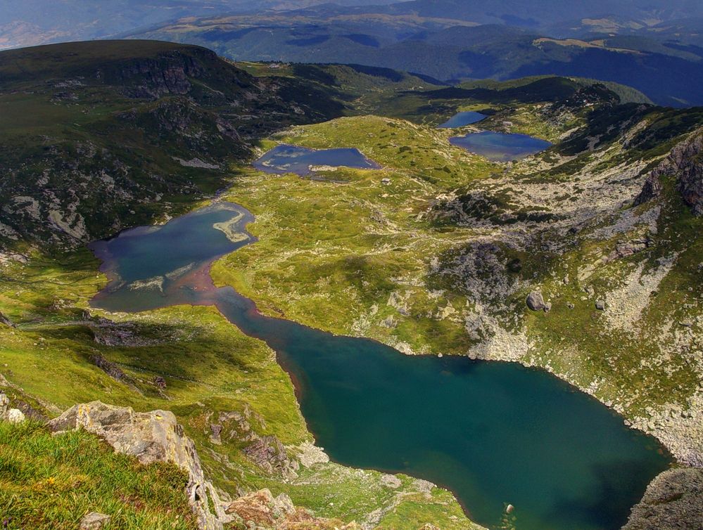 Caption: An aerial view of five of the Seven Rila lakes, Rila mountain, Bulgaria. The water of the lakes is deep blue-green and the surrounding hills are bright green. (Local Guide Mihail Arnaudov)