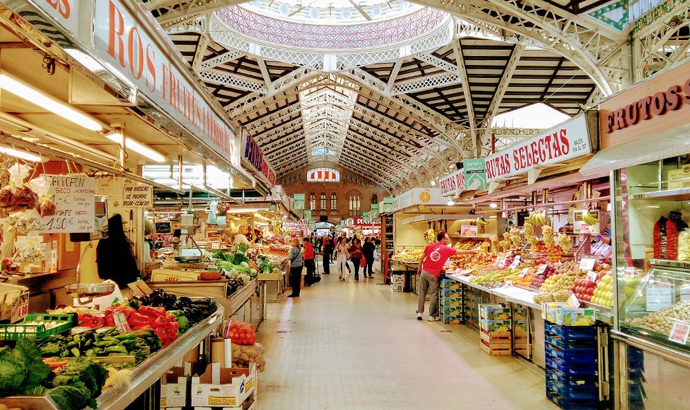 Caption: A wide angle view photo of the Central Market of Valencia with vendors selling food and produce at stalls in Valencia, Spain. (Local Guide Olaf Ritchi VTT)