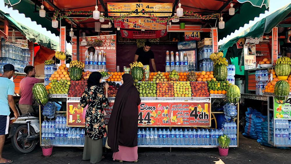 Caption: A photo of women and men shopping at a vendor’s fruit and juice stall in Jemaa el Fna in Marrakech, Morocco. (Local Guide Fernando Paz)