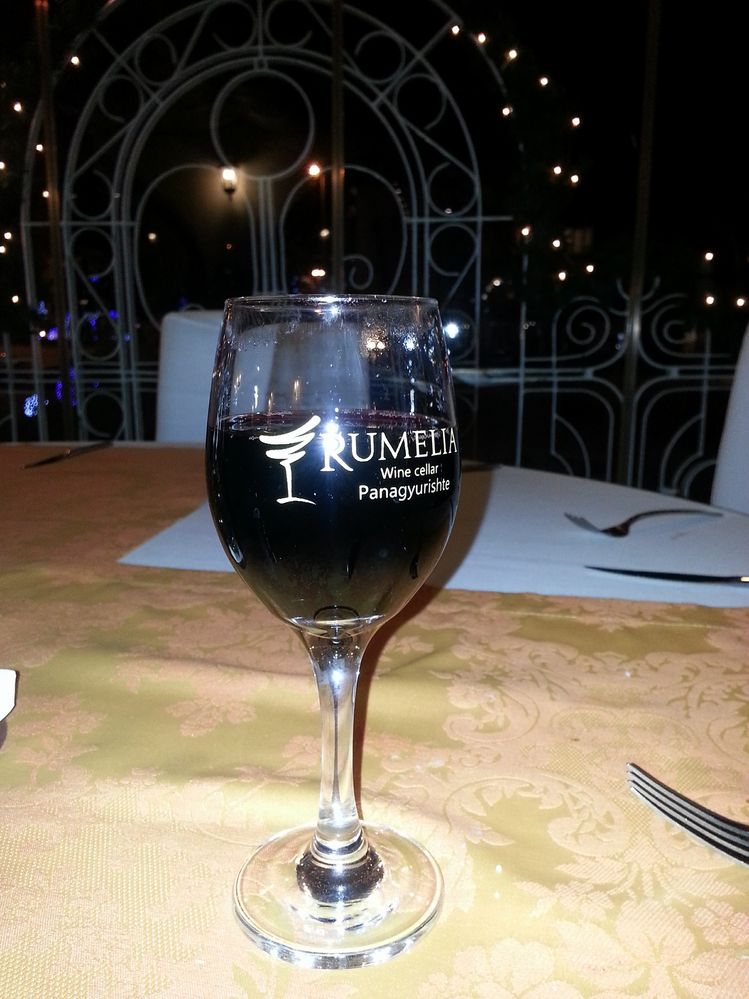 Caption: A photo of a glass of red wine on a table with a sign Rumelia wine celler, Panagyurishte