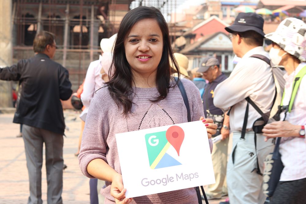 Caption: A photo of Local Guide @SovitaD holding up a sign with the Google Maps logo at a meet-up. (Local Guide @SovitaD)