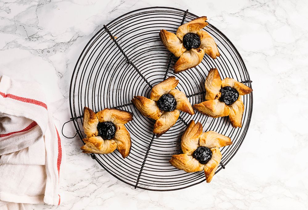 Caption: A photo of a metal tray with five star-shaped “joulutorttu” puff pastries with jam in the center on a white marble countertop. There’s a white and red towel next to the tray. (Getty images)
