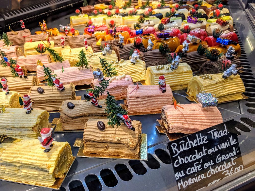 A photo of a display case in a bakery with rows of small bûche de Noël cakes in flavors like traditional chocolate, vanilla, coffee, or Grand Marnier-chocolate with Christmas decorations on top. (Local Guide Robin Rainton)