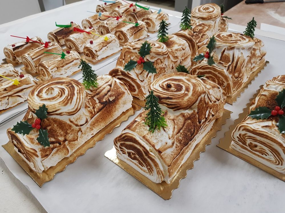 Caption: A photo of large and small bûche de Noël cakes iced in white caramelized meringue topped with Christmas trees, holly, or plastic axes from Boulangerie L'epi D'or Épargnes in Épargnes, France. (Local Guide Nikll Nikll)