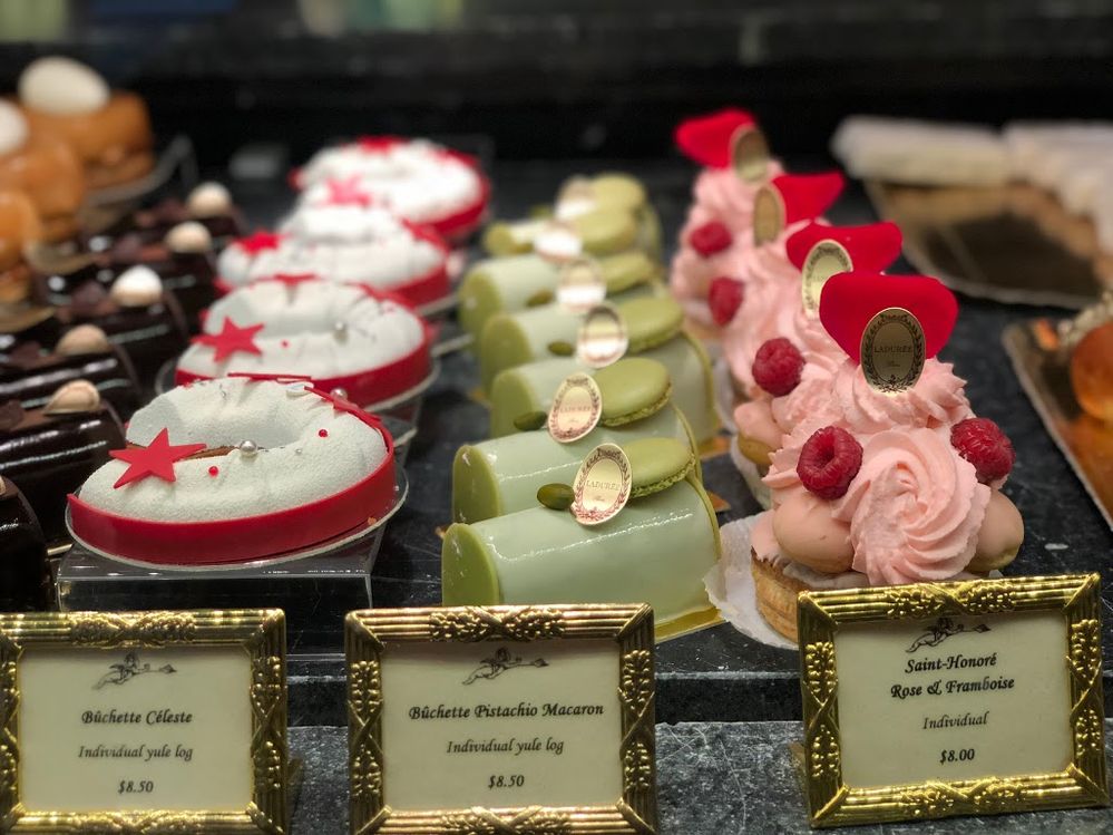 Caption: A photo of rows of mini pistachio bûche de Noël cakes and moon-shaped bûche de Noël cakes alongside St. Honoré cakes at Ladurée in New York City. (Local Guide Ahmad A)