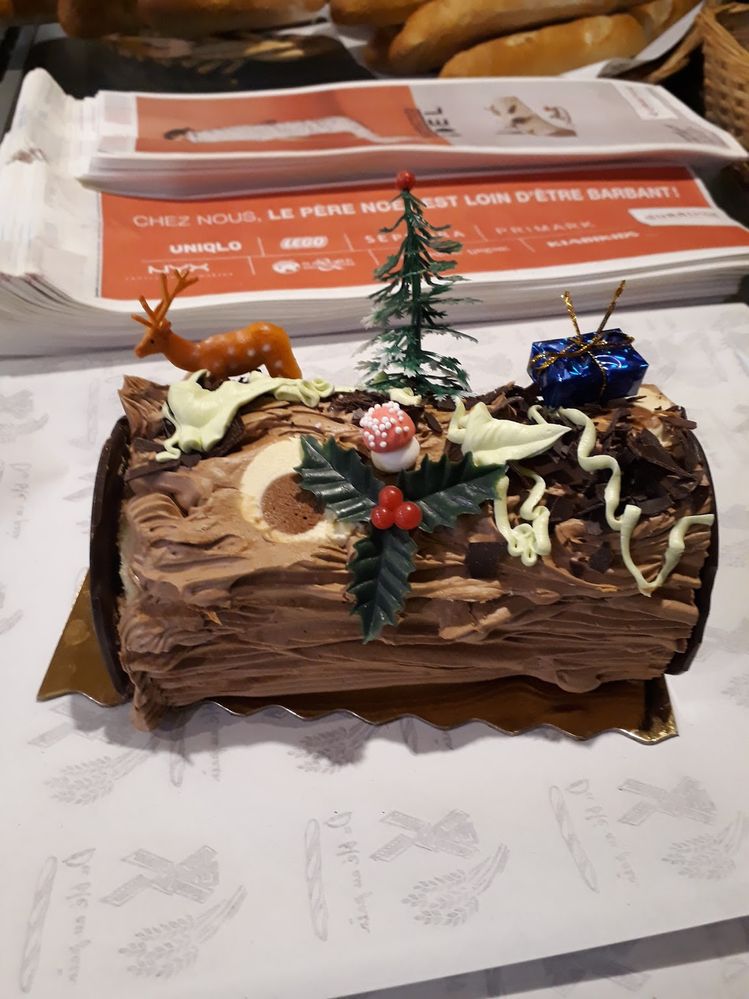 Caption: A photo of a traditional bûche de Noël cake topped with a candy mushroom, holly, a plastic deer toy, a small Christmas tree, and a small present. (Local Guide catherine senechal)