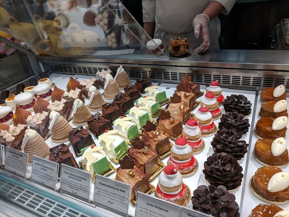 Caption: A photo of rows of pastries and cakes in a display case at Dominique Ansel Bakery in New York, including rows of mini bûche de Noël cakes in flavors like double chocolate, cherry pistachio with a reindeer decoration, and chestnut. (Local Guide Byron)