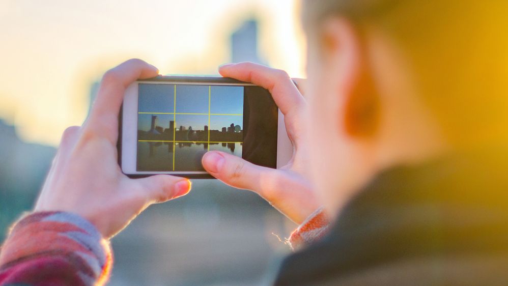 Caption: A closeup photo of a woman taking a photograph of a cityscape, with the camera grid function turned on in her smartphone. (Getty Images)