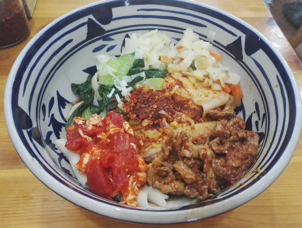 描述：一碗bianbiang面的照片。在碗裡面能看到蕃茄、肉、洋芋、麵條和蔬菜。（在地嚮導 @TsekoV)