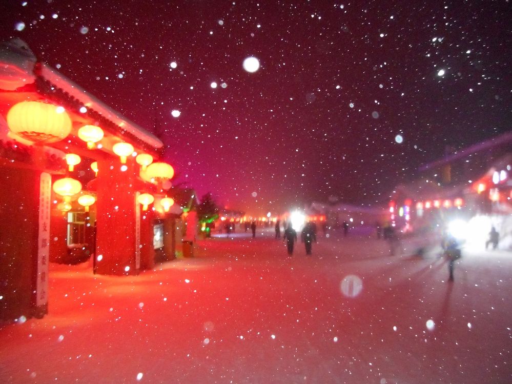 描述：中国雪乡主要步行街的夜景照片。能看到明亮的红色灯笼、模糊的人影和白色的雪花。 (本地向导 @TsekoV)