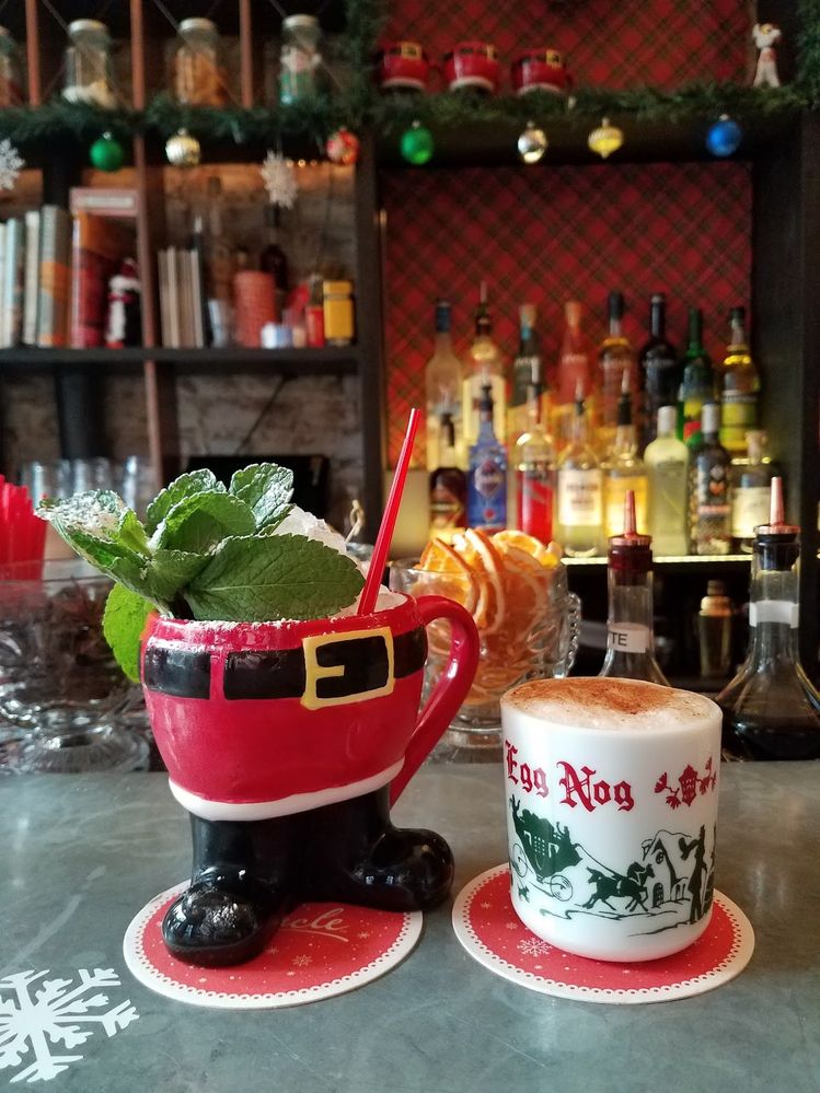 Caption: A photo of a cocktail in a mug in the shape of Santa’s legs and a cocktail in an old-fashioned-looking eggnog mug sitting on the bar at the Christmas pop-up at Mace bar in New York City. (Local Guide Amanda Spurlock)
