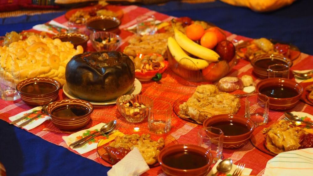 Caption: A photo of a traditional Christmas Eve meal in Bulgaria. There are plates filled with thick bean soup and stuffed peppers, bowls of wine, a loaf of traditional Christmas bread, and fruits. (Local Guide @Ivi_Ge)