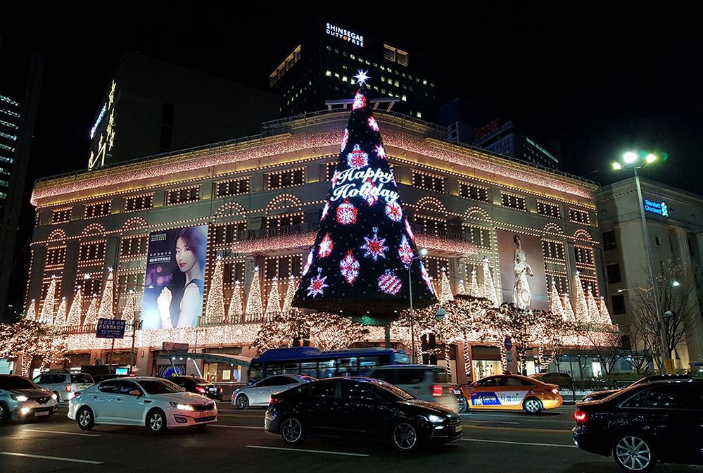 Caption: A night photo of Shinsegae Department Main Store in Seoul, Korea. The building is decorated with Christmas lights and a full-size Christmas tree, with the words “Happy Holiday” written on it. (Local Guide Minjun Choi)