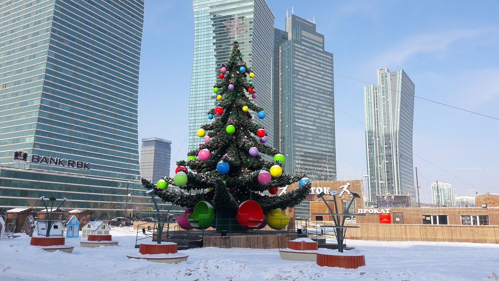 Caption: A photo of a Christmas tree ride in front of modern skyscrapers. Giant ornaments at the bottom double as cars for passengers to sit and ride in Astana, Kazakhstan. (Photo by Local Guide Saba Saba)