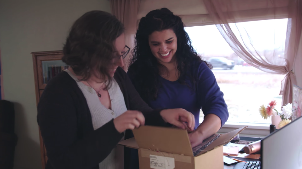 Caption: A screenshot from a YouTube video showing Local Guides Megan Coburn and Grace Johnson opening a box containing the gift they made for Local Guides at the Connect Live summit.