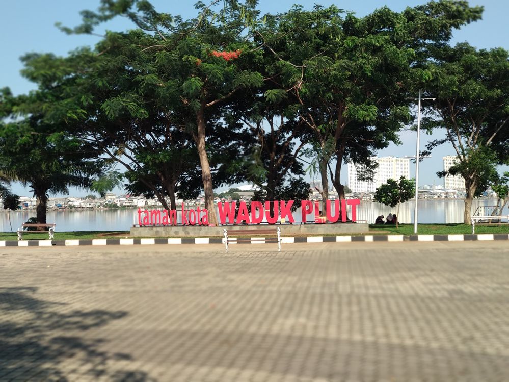 Caption: Foto sederetan huruf besar bertuliskan “taman kota WADUK PLUIT” di bawah pepohonan di Taman Waduk Pluit di Jakarta Utara, Indonesia. (Local Guide Ugahari Nurul)