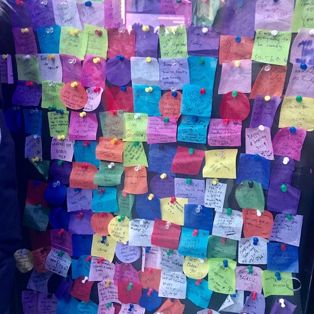 Caption: Various hand-written wishes on colorful squares of confetti are pinned to a wall in Times Square.
