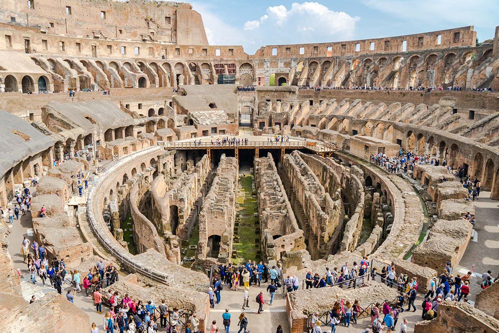 Caption: A wide view photo of the interior of the Colosseum in Rome, Italy, with many people crowded around. (Local Guide Michael Turtle)