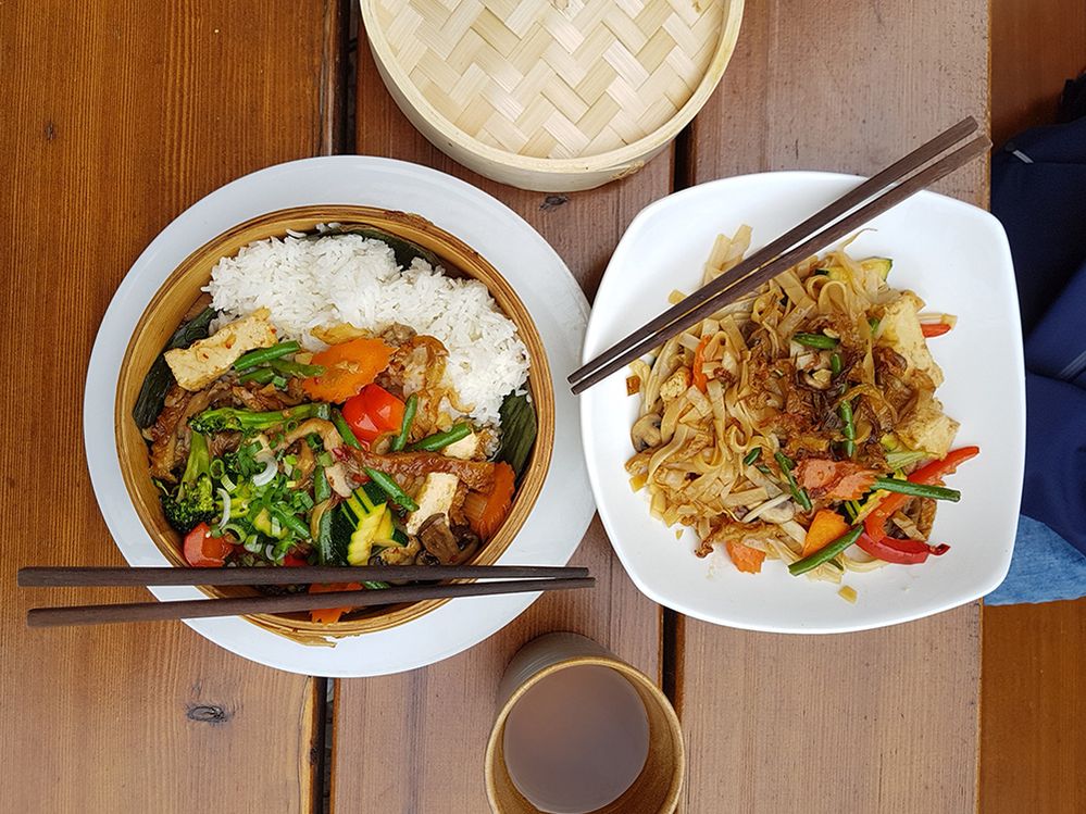 Caption: A photo of two dishes on a table, taken from above. One dish is filled with noodles and vegetables while the other is filled with rice and vegetables. Both have chopsticks resting on top. (Local Guide Oliver VeganBerlin)