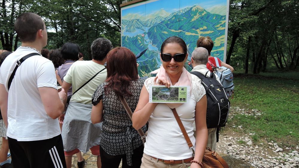 Fotografija Google Moderatora @KatyaL nasmijana i drži veliku ulaznicu za Nacionalni park Plitvička jezera. Iza nje je skupina ljudi koja gleda prema mapi parka na ulazu. (Lokalni vodič @KatyaL)