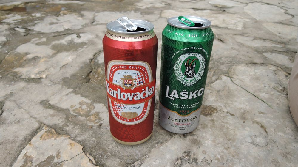 Približna fotografija dvije limenke piva jedna pored druge. S lijeve strane nalazi se crvena limenka Karlovačkog piva, a s desne strane je zelena limenka Laškog piva. (Lokalni vodič @KatyaL)