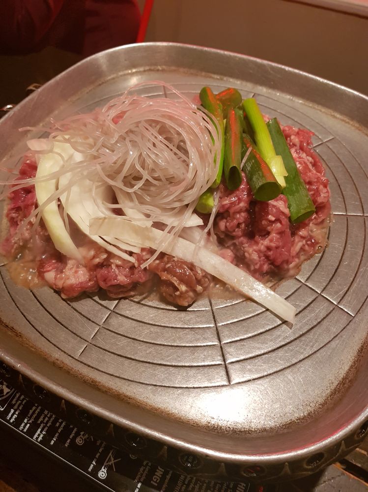 Caption: A photo of a Korean barbecue hot plate with raw minced meat, white and green onion, and glass noodles ready to be cooked. (Local Guide @NadyaPN)