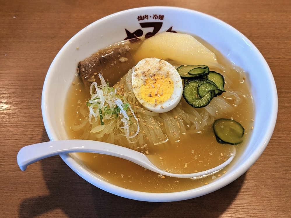 Caption: A photo of a bowl of Morioka Reimen, a soup with rice noodles, beef stock, beef, Japanese onion, sliced-cucumber, a boiled egg, kimchi, and fruit. (Local Guide @HiroyukiTakisawa)