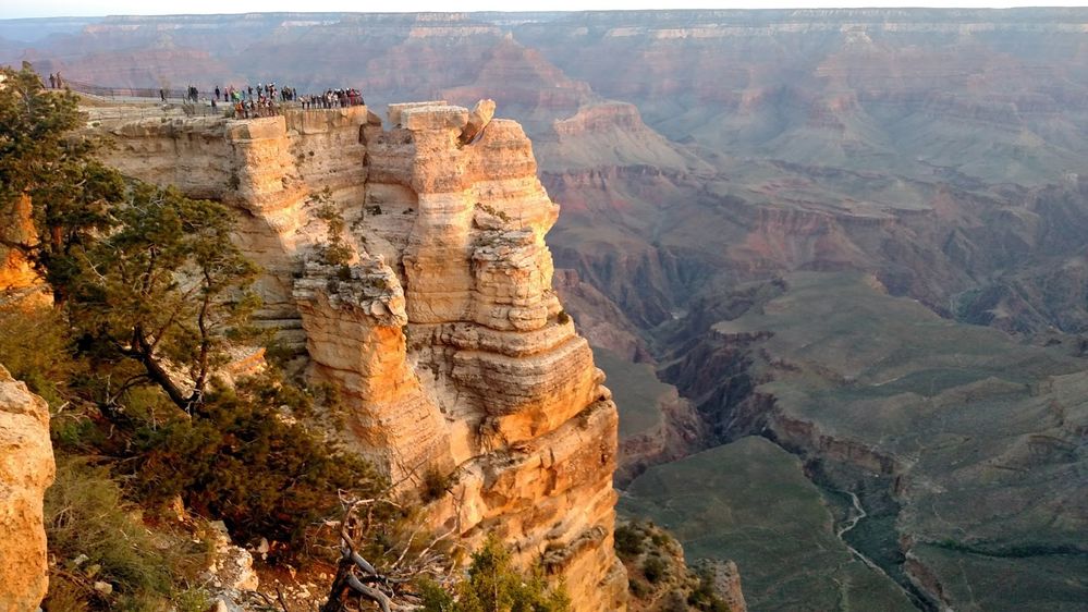 Caption: A photo of Mather Point in the Grand Canyon in Arizona, showing people on a viewing platform on top of a high cliff surrounded by a fence and the canyon below. (Local Guide Tim Kelly)