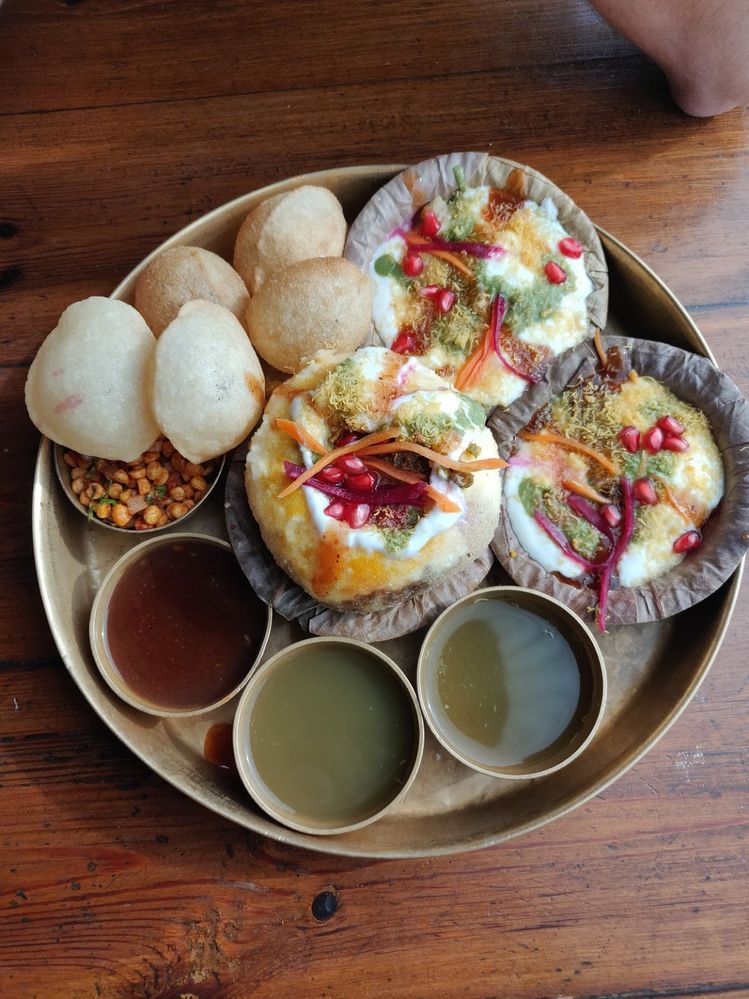 Caption: A photo of a circular tray holding smaller circular plates containing colorful dishes of food and sauces as well as puffed dough on the side. (Local Guide Jagrit Chhabra)