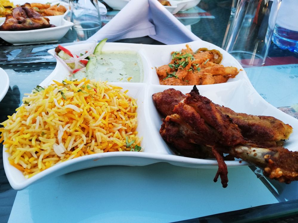 Caption: A photo of a white plate with four sections containing rice, meat, a green sauce, and fried potatoes at The Monal in Islamabad, Pakistan. (Local Guide Muhammad Junaid)