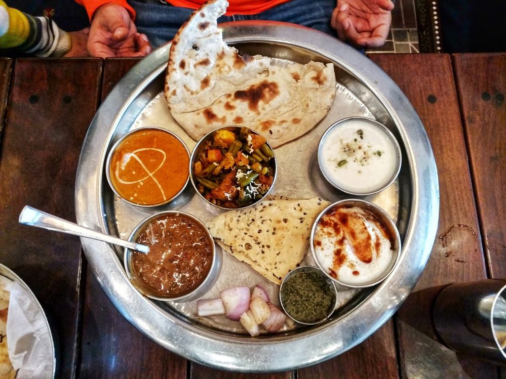Caption: A photo of a large, circular silver tray with small circular dishes on it containing different food and sauces along with some naan bread. (Local Guide Paras Suri)
