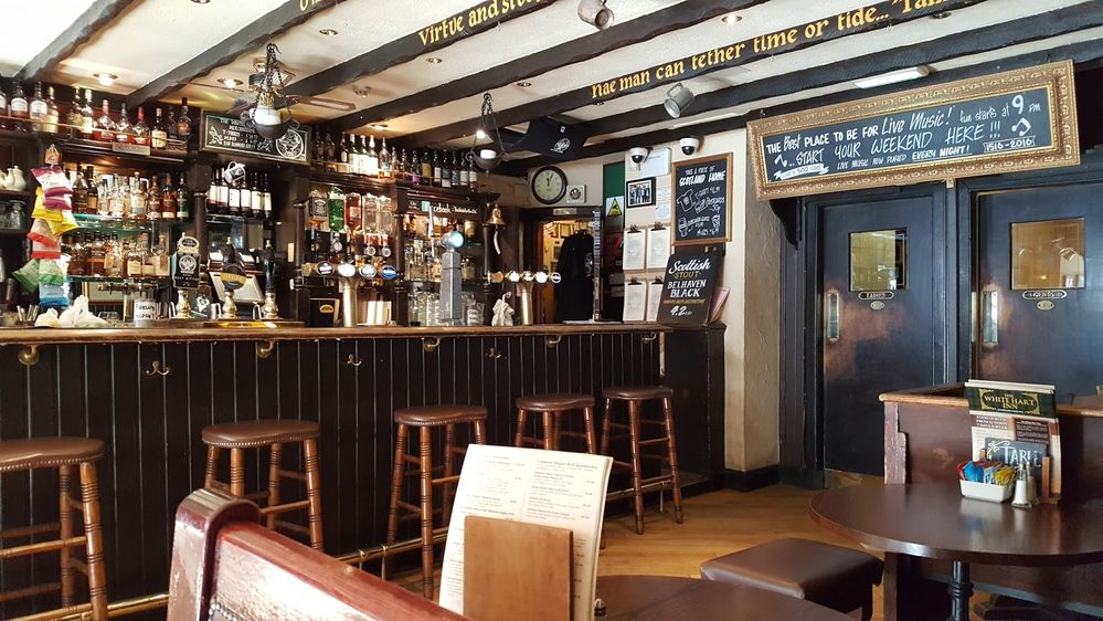 Caption: A photo of the interior of The White Hart Inn in Edinburgh showing the wooden bar filled with glass liquor bottles and the wooden ceiling beams that have verses from poems by Robert Burns painted on them in gold. (Local Guide Caitlin Campbell)